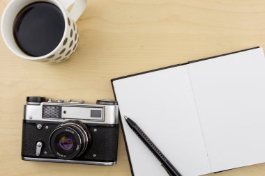 Eski fotoğraf makinesi, defter, kalem ve bir fincan kahve ahşap yüzey üzerinde