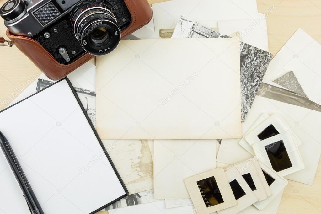 Old camera, notebook and pen on stack of photos and transparency