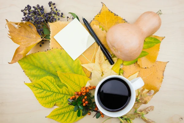 Une tasse de café et une note avec bouquet de feuilles d'automne jaunes et vertes, de baies et de graines . — Photo