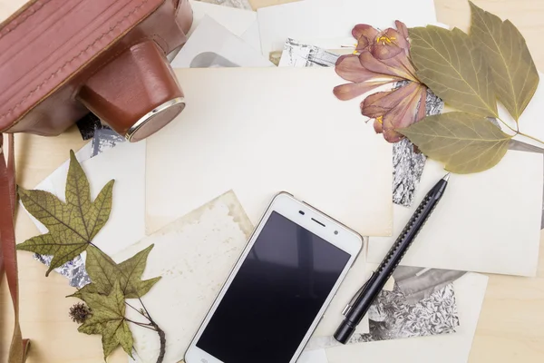 Old camera and smartphone on stack of photos with dry plants, on wooden surface. — Stock Photo, Image