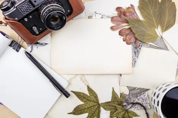 Câmera velha em pilha de fotos com notebook, caneta e plantas secas — Fotografia de Stock