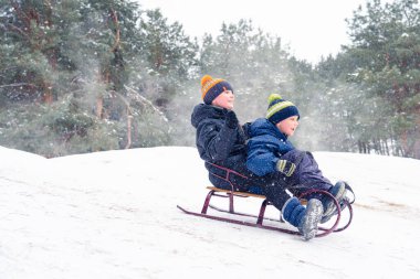 Çocuklar karlı bir ormanda kızak kayıyor. Noel tatili için açık hava kış eğlencesi.