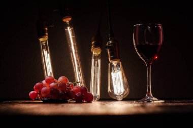 Şarap ve üzümlü şarap kadehi, yakınlardaki koyu ahşap bir masada, arka planda bir Edison lambasının önünde.