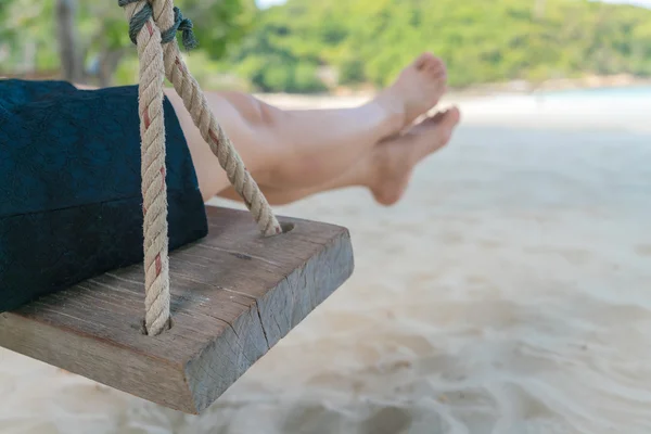 Kvinnan lägger benen på ryggen på en gunga på tropiska havet beach — Stockfoto