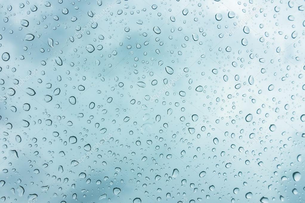 Drops of water on glass window over blue sky .