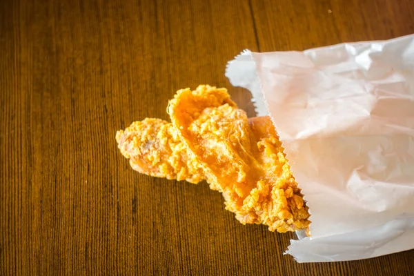 Жареные куриные крылышки в бумажном пакете на деревянном столе  . — стоковое фото