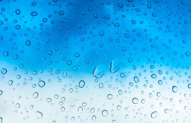 Mavi gökyüzü üzerinde cam pencere üstünde su damlaları .