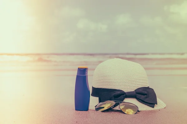 Sunglasses, sun cream and hat  on white  sand beach - Filtered i — Stock Photo, Image
