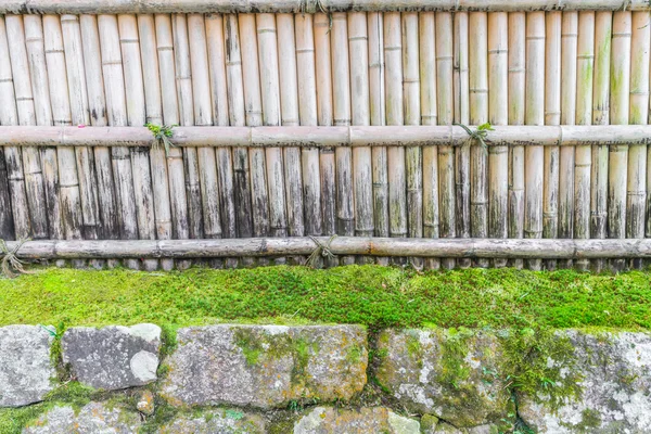 Bambusový plot na kameni se zelenými listy  . — Stock fotografie