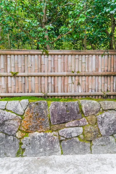 Bambusový plot na kameni se zelenými listy  . — Stock fotografie