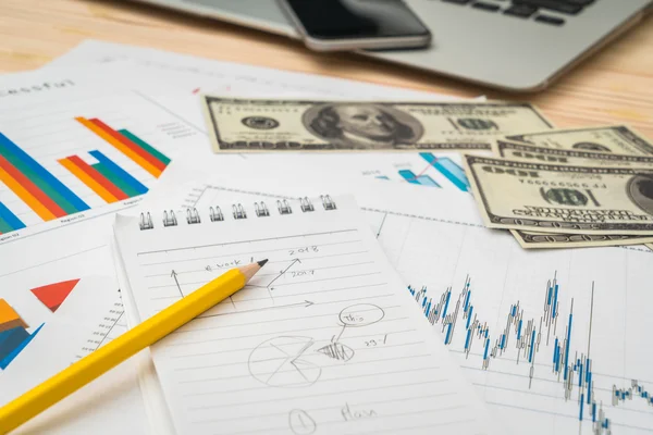 Gráficos financeiros em cima da mesa com laptop, telefone, dólares bankn — Fotografia de Stock