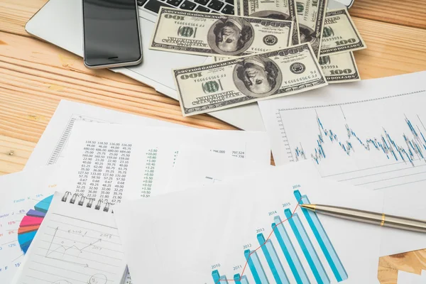 Grafici finanziari sul tavolo con laptop, telefono, banca dollari — Foto Stock