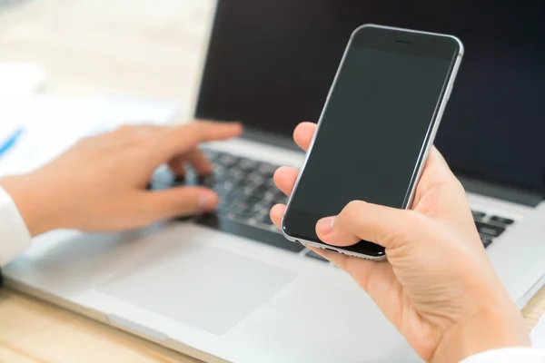 Gros plan de téléphone tactile main femme d'affaires sur le clavier de l'ordinateur portable — Photo