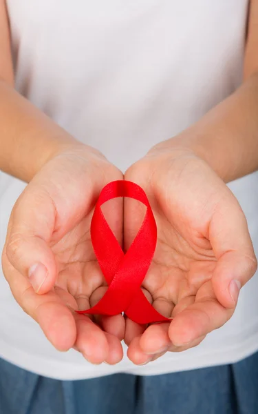 Mãos femininas segurando fita vermelha da consciência da AIDS — Fotografia de Stock