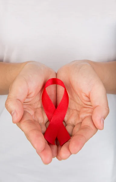 Mãos femininas segurando fita vermelha da consciência da AIDS — Fotografia de Stock