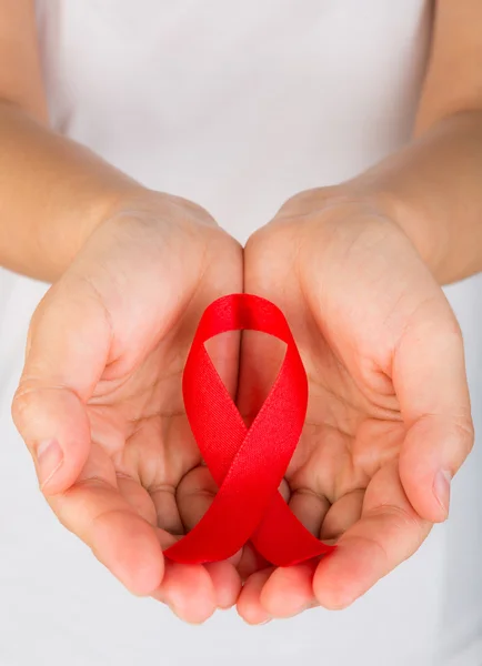 Mãos femininas segurando fita vermelha da consciência da AIDS — Fotografia de Stock