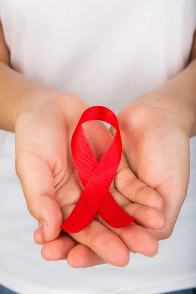 Mãos femininas segurando fita vermelha da consciência da AIDS — Fotografia de Stock