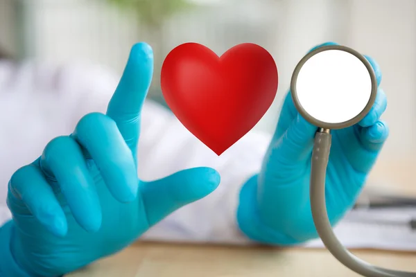 Médico con estetoscopio y corazón rojo en la mano —  Fotos de Stock