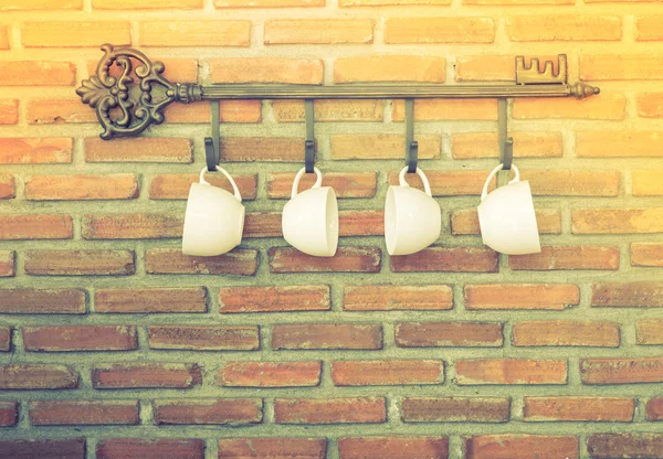 Tasses à café suspendues aux crochets devant le mur de briques (Filtré i — Photo