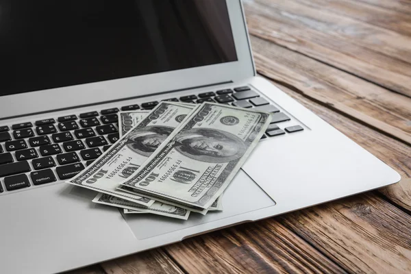 Laptop and one hundred dollar banknotes on wooden table. — Stock Photo, Image