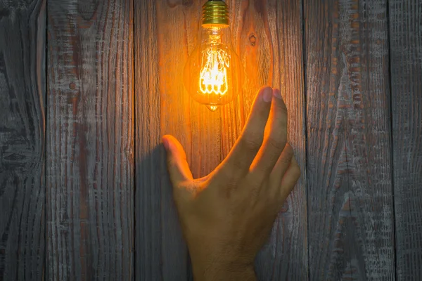 Hand mit glühender Glühbirne auf dem Holzgrund — Stockfoto