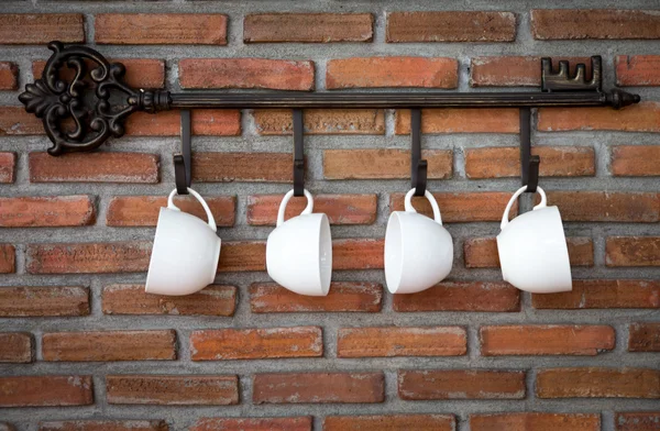 Tazas de café colgando de ganchos delante de la pared de ladrillo —  Fotos de Stock