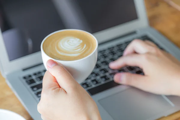 Закрытие руки деловой женщины, печатающей на клавиатуре ноутбука и кофеварке — стоковое фото