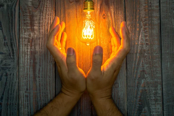 Mão com lâmpada brilhante no fundo de madeira — Fotografia de Stock