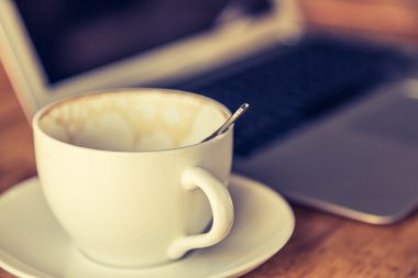 Boş kahve fincanı ve eski ahşap masa üstünde laptop