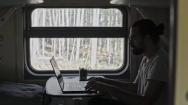 Trendeki adam bilgisayarın üzerinde çalışıyor. Dizüstü bilgisayarın klavyesindeki metni yazdırır. Trende serbest çalışan turistler. Sınırları genişletiyorum. Hareket eden bir trende sallanırken.