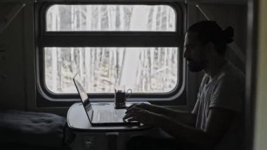 Trendeki adam bilgisayarın üzerinde çalışıyor. Dizüstü bilgisayarın klavyesindeki metni yazdırır. Trende serbest çalışan turistler. Sınırları genişletiyorum. Hareket eden bir trende sallanırken.