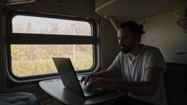 Trendeki adam bilgisayarın üzerinde çalışıyor. Dizüstü bilgisayarın klavyesindeki metni yazdırır. Trende serbest çalışan turistler. Sınırları genişletiyorum. Hareket eden bir trende sallanırken.