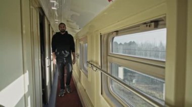 Trenin penceresinde genç ve yakışıklı bir adam duruyor. Tren penceresinin dışındaki manzara. Uzağa bak. Uzun saçlı ve sakallı bir adam, seyahatte olan bir turist..