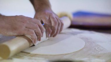 Genç yakışıklı aşçı evde yemek yapıyor. Önlüklü bir şef hamuru ince ince yuvarlıyor. Bir aşçının ve hamurun yakın çekimi. Malzemeler masada. Erişte için Hamur..