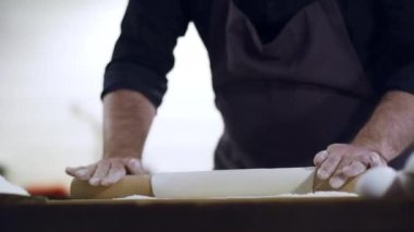 Genç yakışıklı aşçı evde yemek yapıyor. Önlüklü bir şef hamuru ince ince yuvarlıyor. Bir aşçının ve hamurun yakın çekimi. Malzemeler masada. Erişte için Hamur..