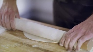 Genç yakışıklı aşçı evde yemek yapıyor. Önlüklü bir şef hamuru ince ince yuvarlıyor. Bir aşçının ve hamurun yakın çekimi. Malzemeler masada. Erişte için Hamur..