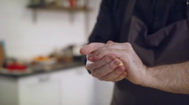 Genç yakışıklı aşçı mutfakta hamur hazırlıyor. Önlüklü şef hamuru yoğurur. Bir aşçının elinin yakın çekimi. Un masanın üzerine saçılmış. Malzemeler masanın üstünde..