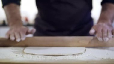 Genç yakışıklı aşçı evde yemek yapıyor. Önlüklü bir şef hamuru ince ince yuvarlıyor. Bir aşçının ve hamurun yakın çekimi. Malzemeler masada. Erişte için Hamur..