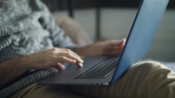 Joven hombre guapo trabajando en un ordenador portátil mientras está acostado en la cama. — Vídeo de stock