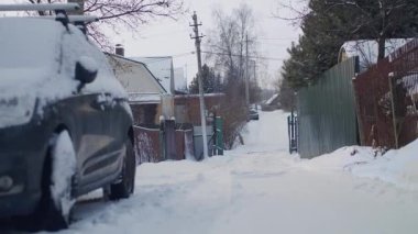 Kışın bir köy sokağında karla kaplı araba.