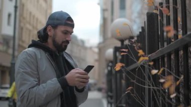 Güneşli bir sonbahar gününde, şehir sokağında telefonu olan genç yakışıklı bir adam..