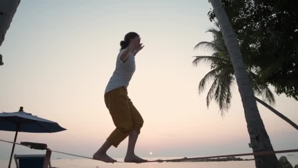 La chica va en un slackline al atardecer en una playa tropical. — Vídeos de Stock