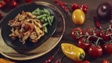 Tahta masada en iyi plan hazır. Masaya taze sebzelerle süslenmiş bir tabak yiyecek konur. Biber, domates, marul, fasulye kabuğu ve soğan. Düz siyah bir tabakta Udon.