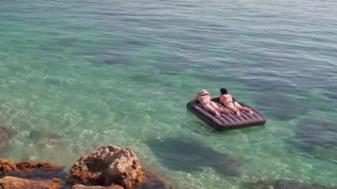 İki kadın denizde şişme bir yatakta güneşleniyorlar.. 