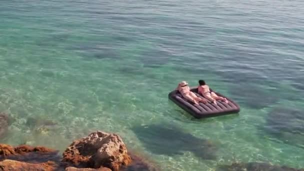 Duas mulheres estão tomando banho de sol deitado em um colchão inflável no mar. — Vídeo de Stock