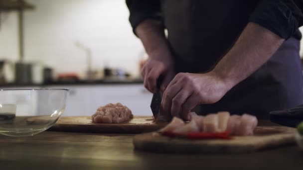 Giovane cuoco carino taglia carne di pollo su una tavola di legno alla cucina di casa. — Video Stock