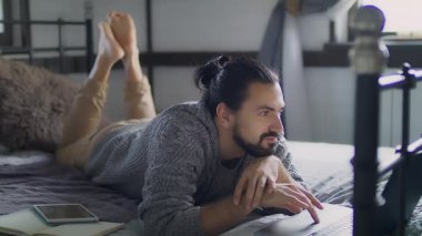 Genç ve yakışıklı bir adam yatakta yatarken dizüstü bilgisayarda çalışıyor.. 