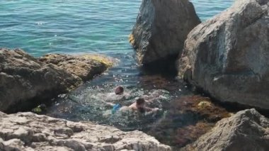 Turistler açık Karadeniz 'de güneşli bir yaz gününde kayaların arasında yüzerler..