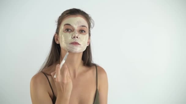 Uma menina bonita jovem aplica uma máscara hidratante em seu rosto com um pincel. — Vídeo de Stock