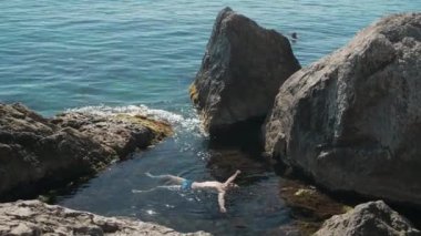 Turistler açık Karadeniz 'de güneşli bir yaz gününde kayaların arasında yüzerler..